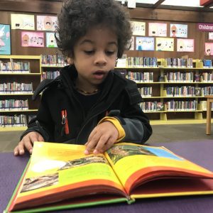 young boy practicing being a successful reader by reading at the library