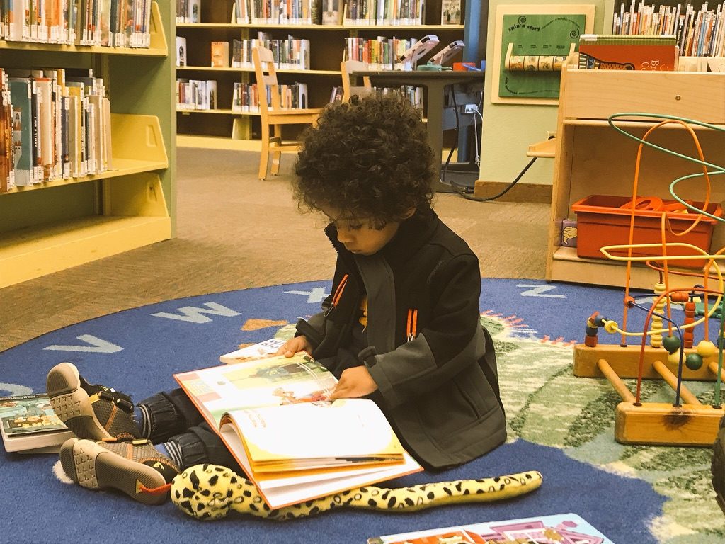 young boy engaged in reading a book on the library floor.  