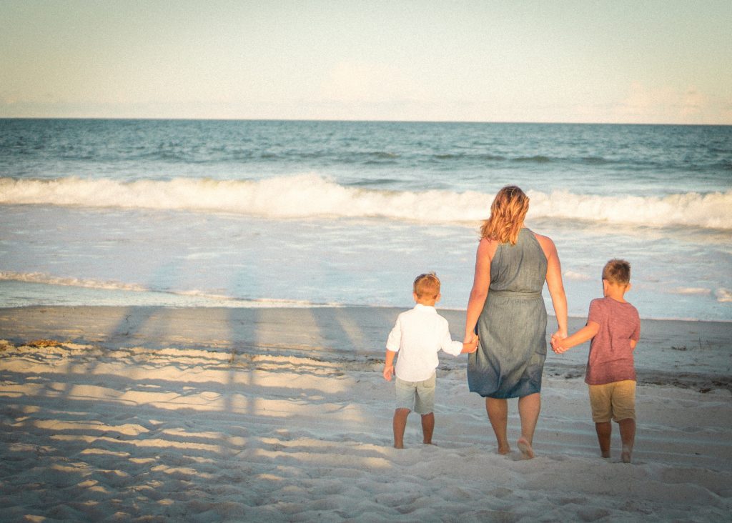 mom and two little boys holding hands exploring an ocean beach being together