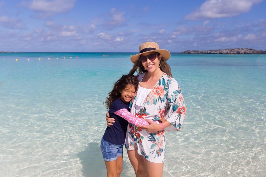 mom and daughter hugging and happy while standing in shallow water  on a warm beach