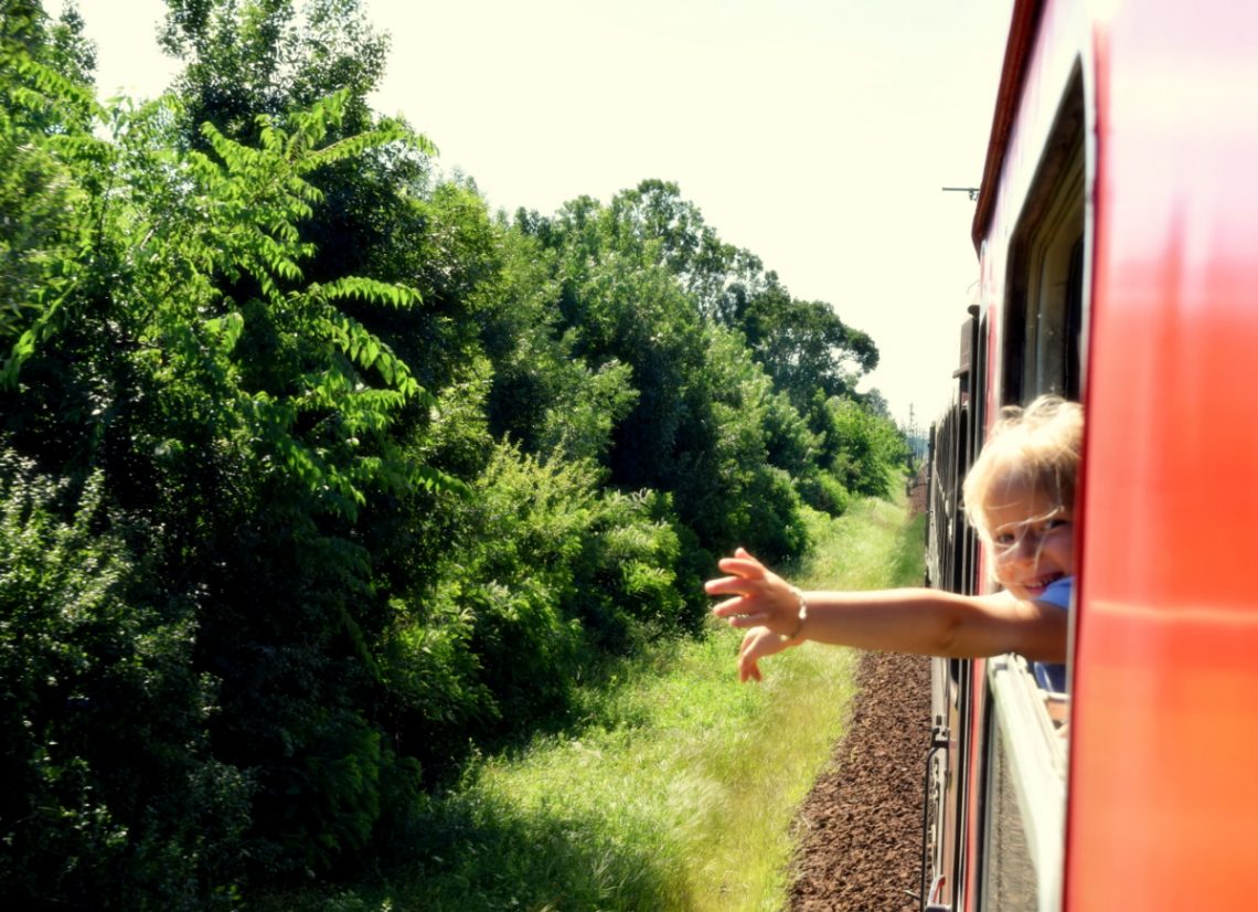 young child sticking their hand out a train window as it travels