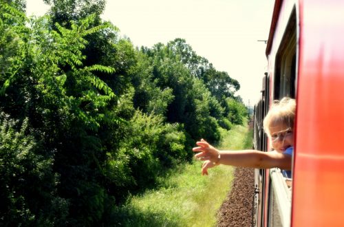 young child sticking their hand out a train window as it travels