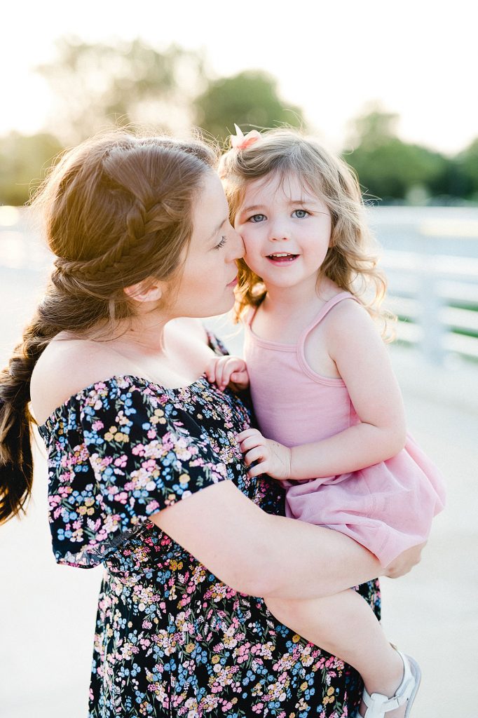 Pregnant mommy holding her toddler daughter and giving her a kiss