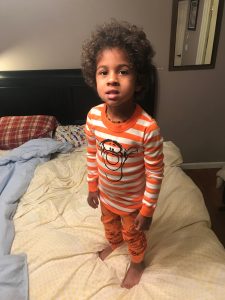 A young boy in his pajamas standing on the family bed for co-sleeping 