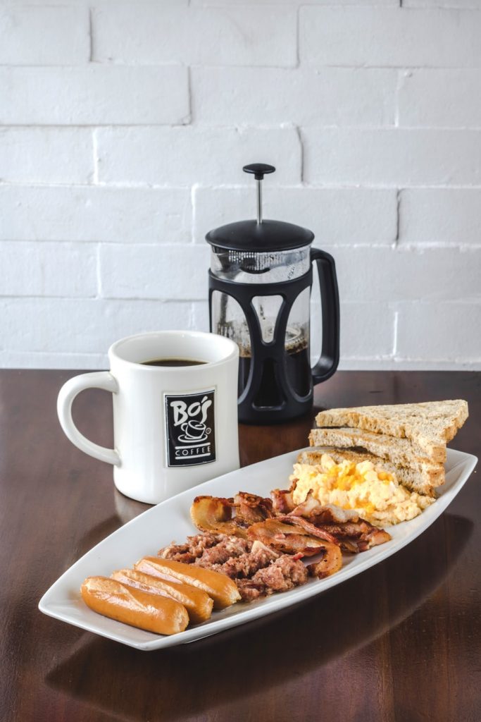 A French coffee press, a mug of black coffee and egg and hash, toast breakfast