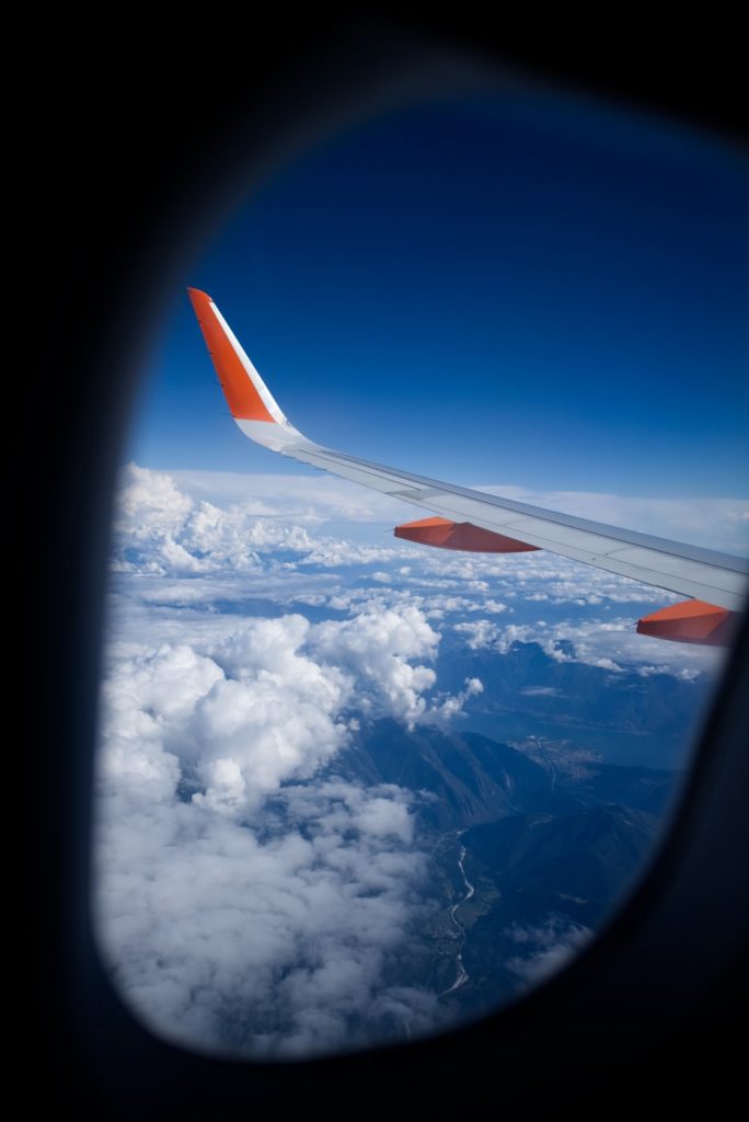 View of the blue skies, clouds and an airplane wing from sitting inside the plane while traveling with kids