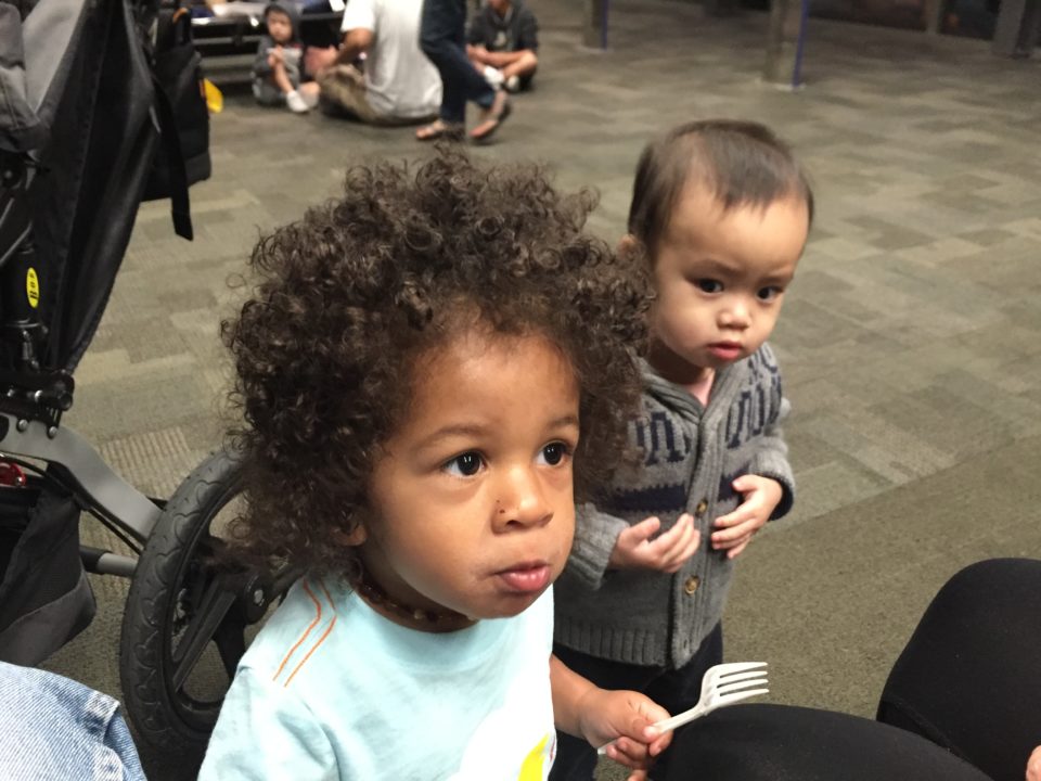 Two toddlers with parents at the airport waiting to fly with kids.  