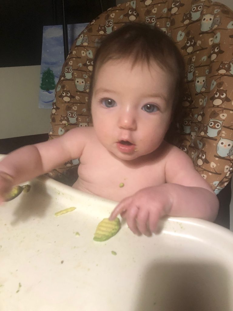 A baby eating chopped up soft finger foods in a high chair. 