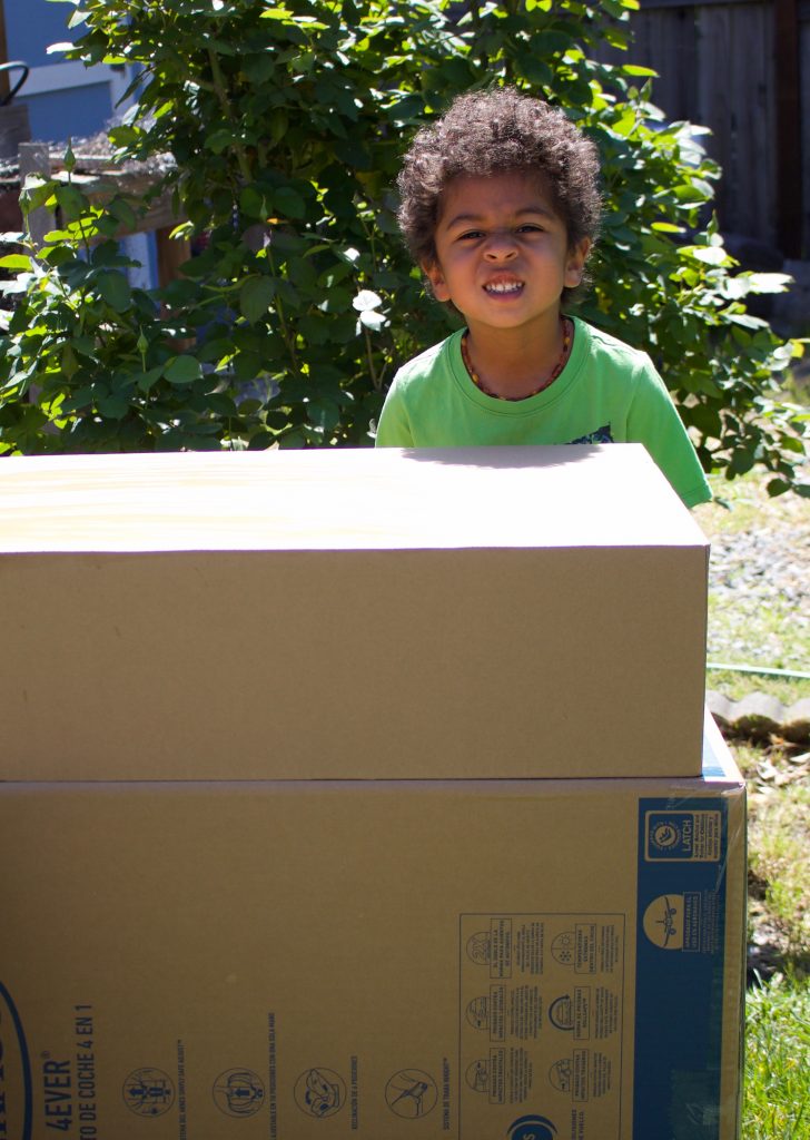 A little boy building with cardboard boxes outdoors on a sunny day 