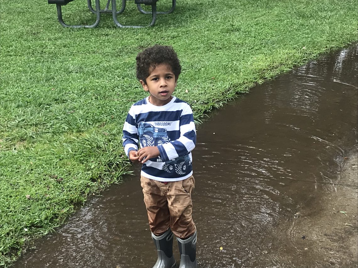 A boy playing outdoors on a rainy day near puddles