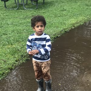 A boy playing outdoors on a rainy day near puddles