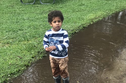 A boy playing outdoors on a rainy day near puddles