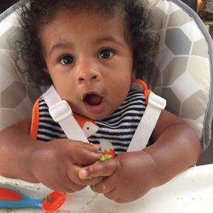 A baby eating soft finger foods while sitting in a high chair