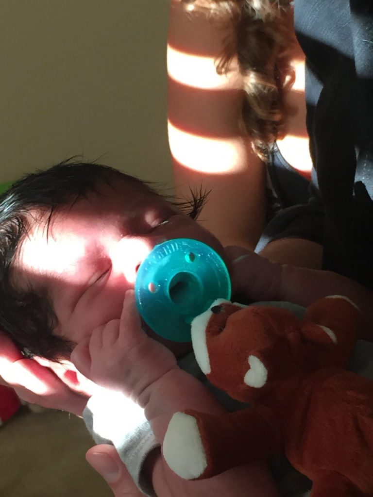 woman holding an infant sucking on a pacifier. 