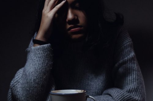 A women in a dark room holding her head drinking tea