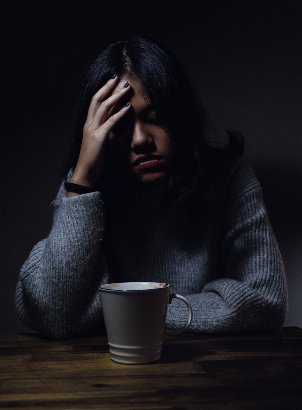 A women in a dark room holding her head drinking tea