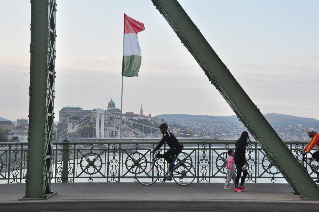 a bridge in Europe with an Italian flag, multiple people walking and biking on the bridge