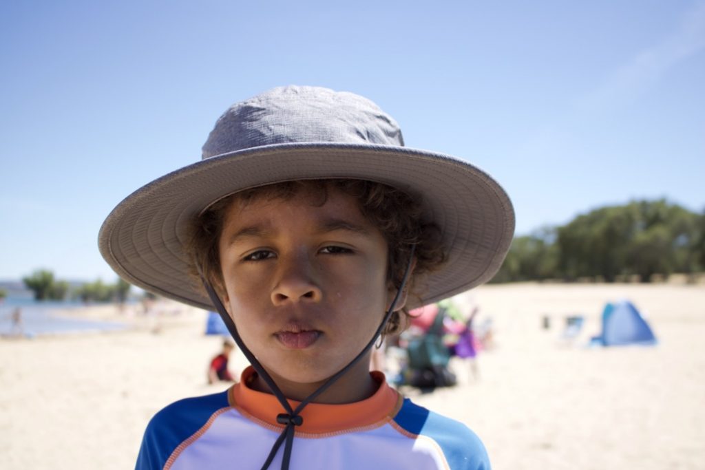 kid at the beach wearing a sun hat, blue white and orange shirt