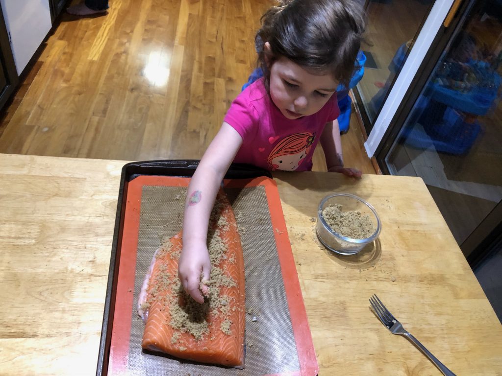 four year old girl in kitchen helping put brown sugar seasoning on salmon