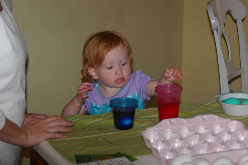 toddler girl with red hair in purple shirt helping her mom make eggs at the table