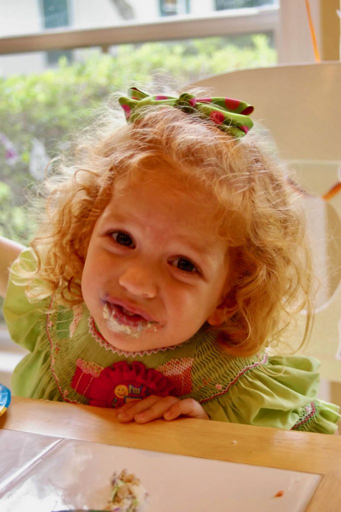 young redhead toddler in lime dress eating at the table after cooking with her mom