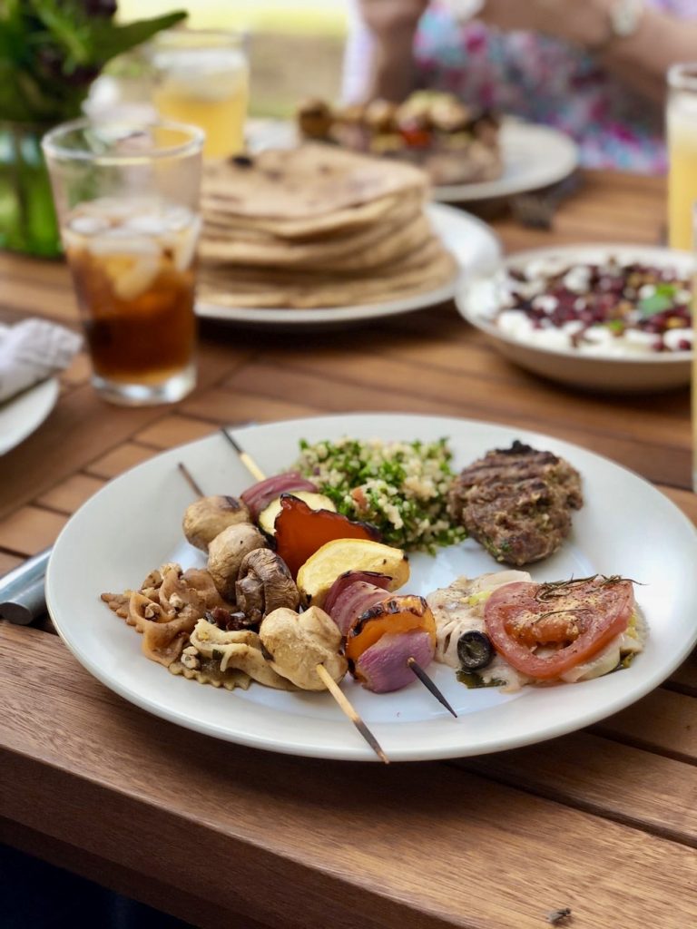 dinner table set outdoors with kebabs and pita bread on white plates