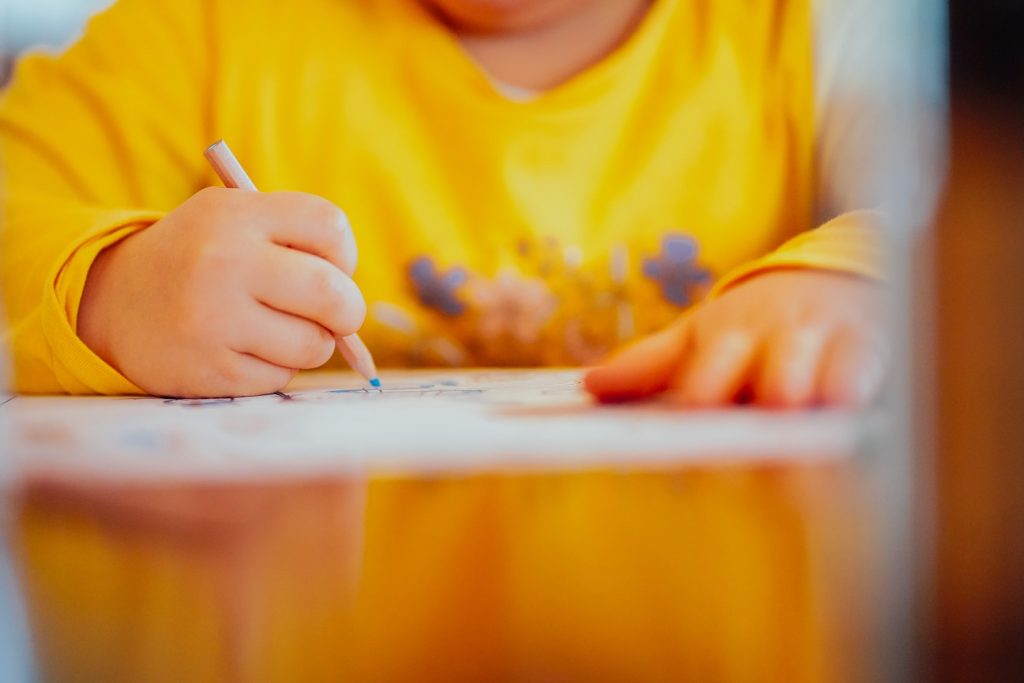 boy in yellow shirt using coloring pencils on paper