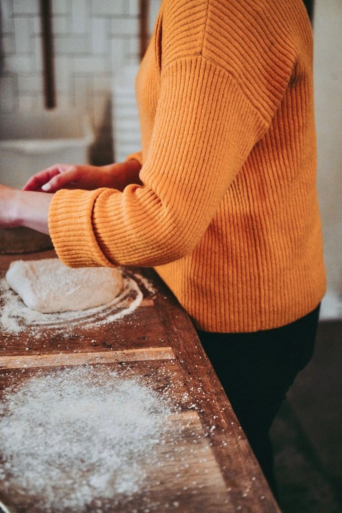 lady in kitchen wearing an orange shirt making pizza dough on wooden table