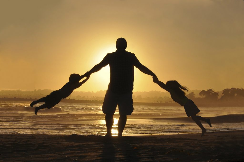 man playing with girl and boy on the beach during a sunset