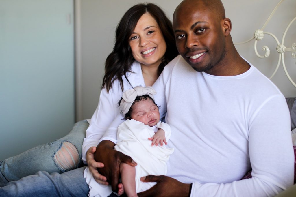 dad and mom wearing white tops taking a family photos with their newborn baby girl. Photo by Eric Ibekwem