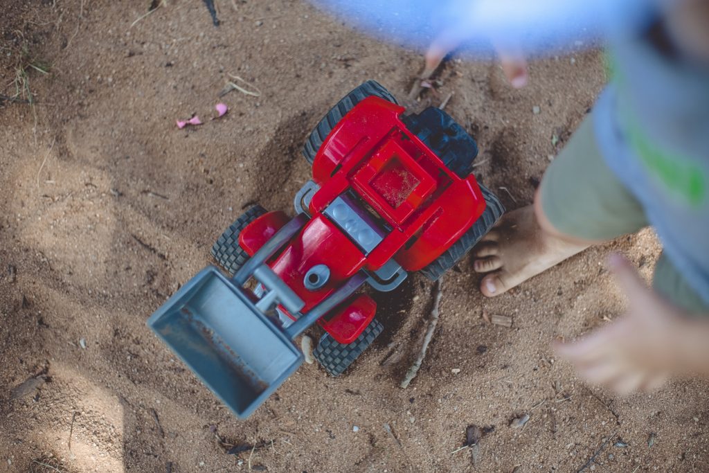 you boy in shorts playing with red bull dozer in the dirt having a scree free zone