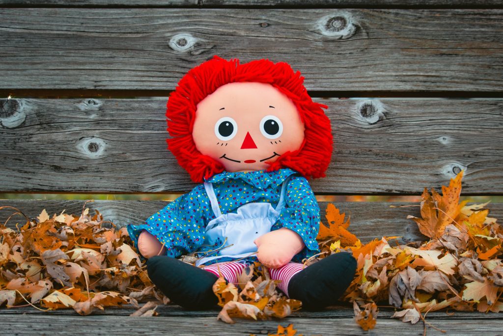 Raggedy Ann doll sitting on bench with leaves