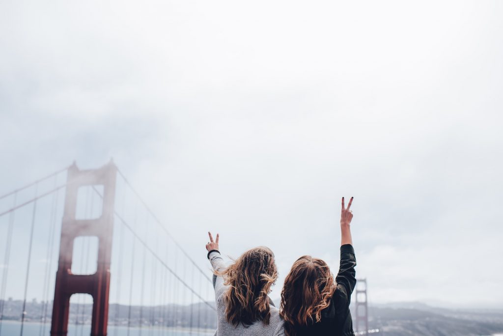 Two people who have traveling in San Francisco, CA taking a photo with the Golden Gate Bridge