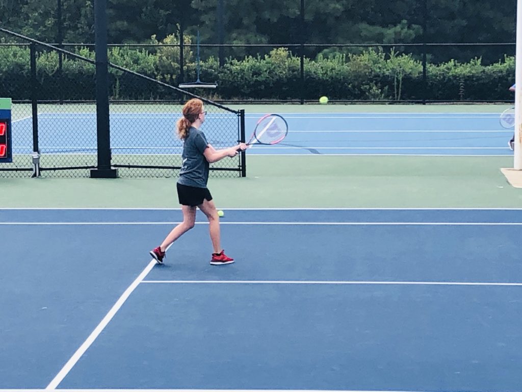 girl on blue tennis court hitting a green tennis ball