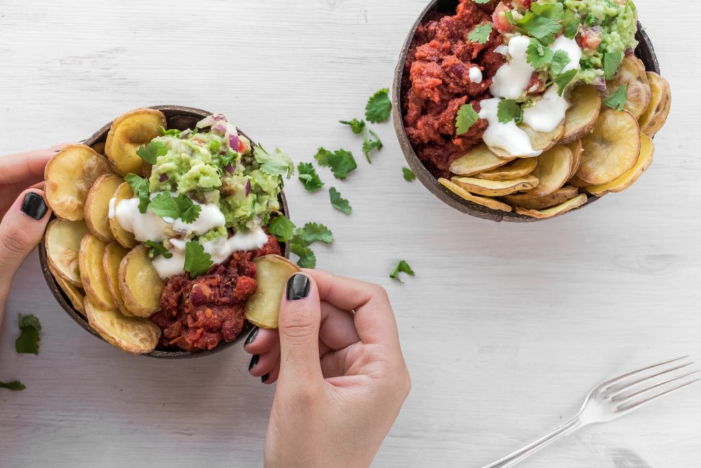 Two bowls of Chili, sour cream, potatoes, and guac.