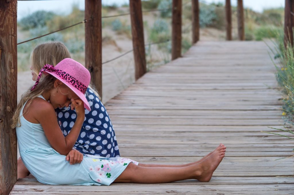 two girls sitting on a dock with one girl hand on head